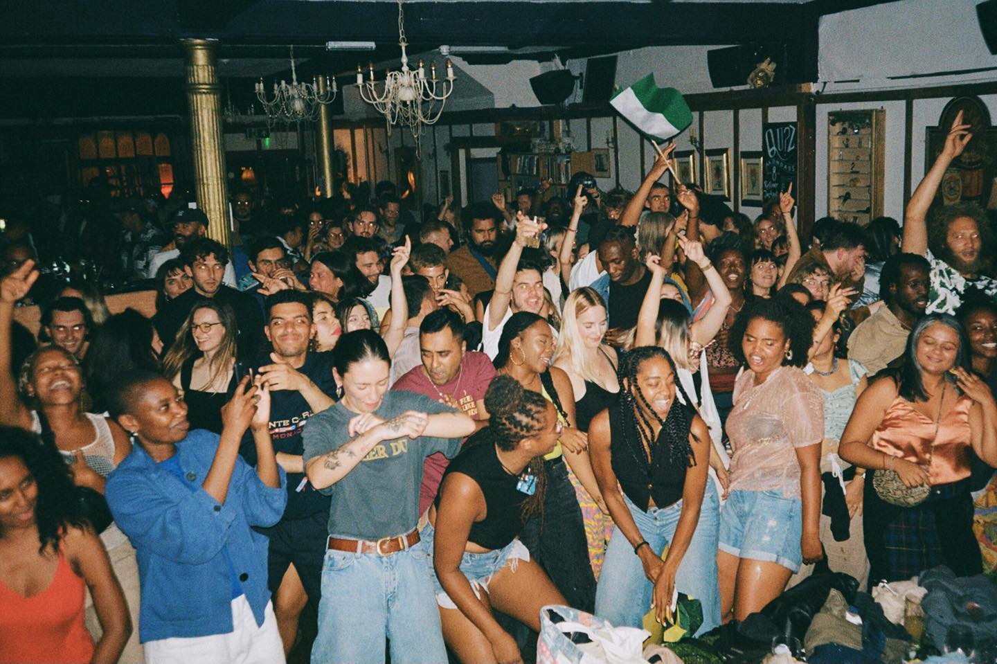 An enthusiastic audience, different members with eyes closed and arms raised, dancing in an indoor space